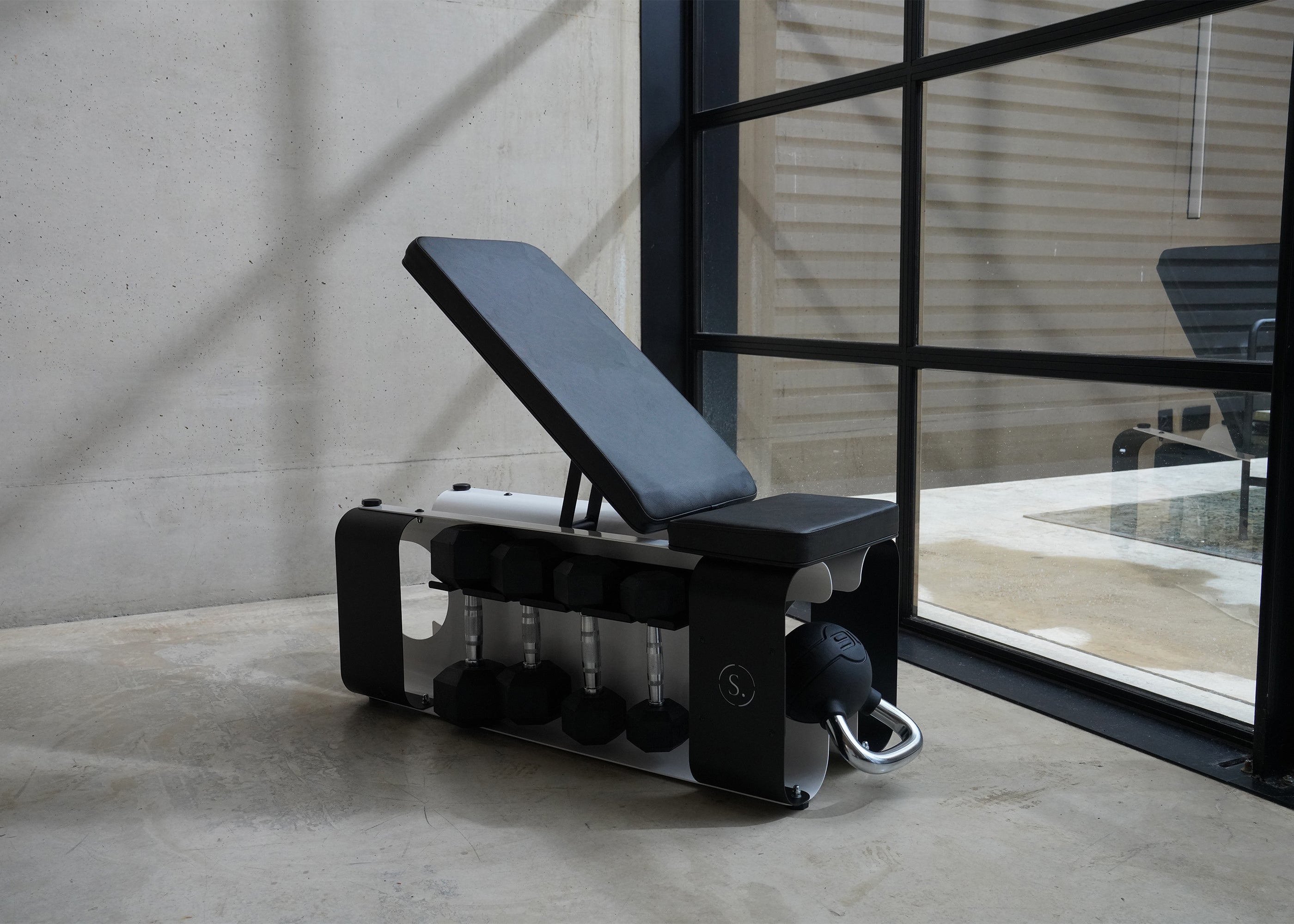 weights bench on a concrete floor with dumbbells and kettlebells inside