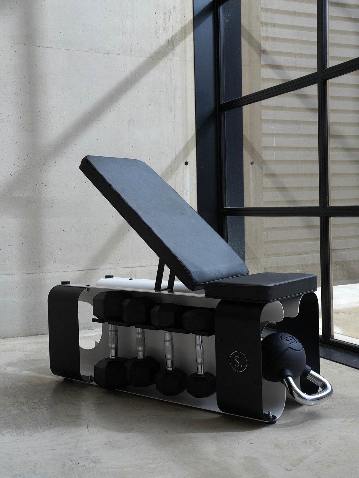 weights bench on a concrete floor with dumbbells and kettlebells inside